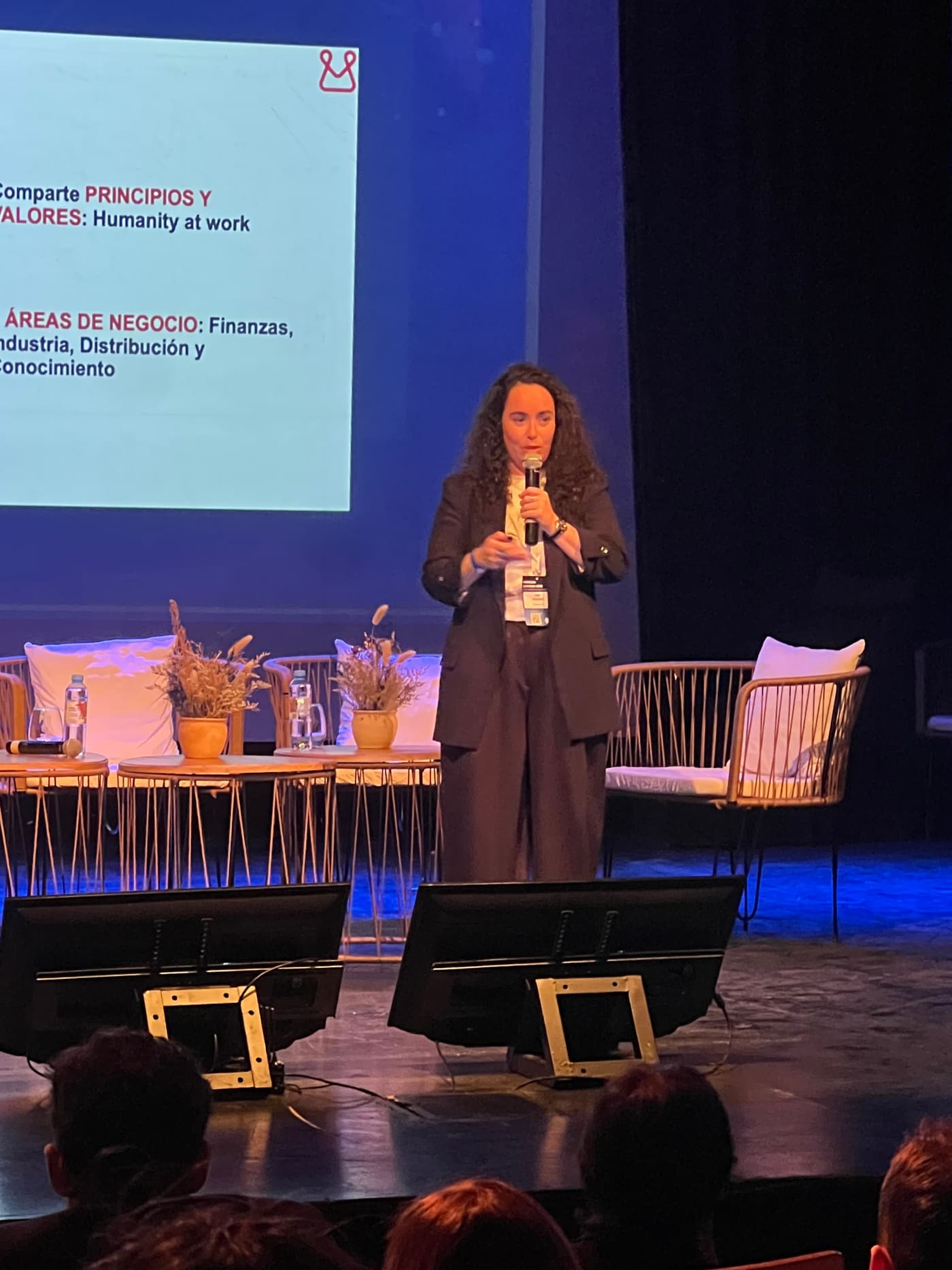 Oradora con micrófono en el escenario, junto a una pantalla con la presentación sobre Mondragón